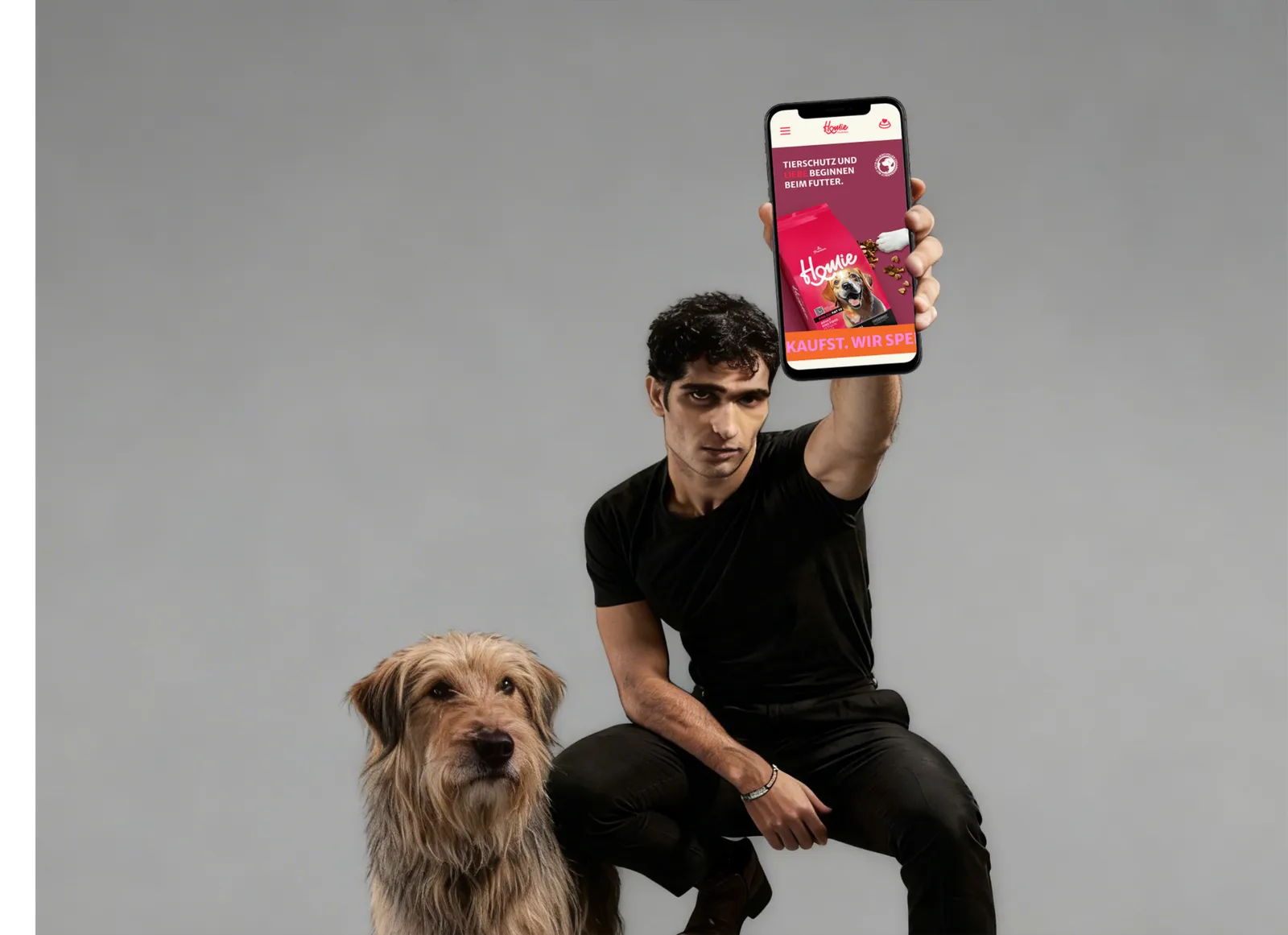 Person holding a phone showing the Homie store, next to a dog